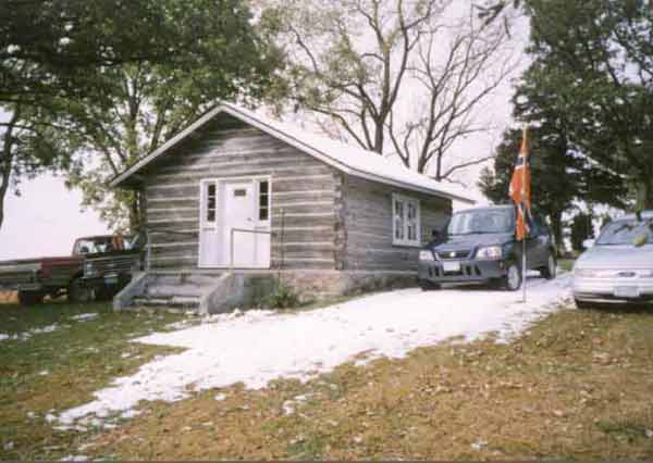 Photo of the log cabin in the spring with the snow almost melted.
